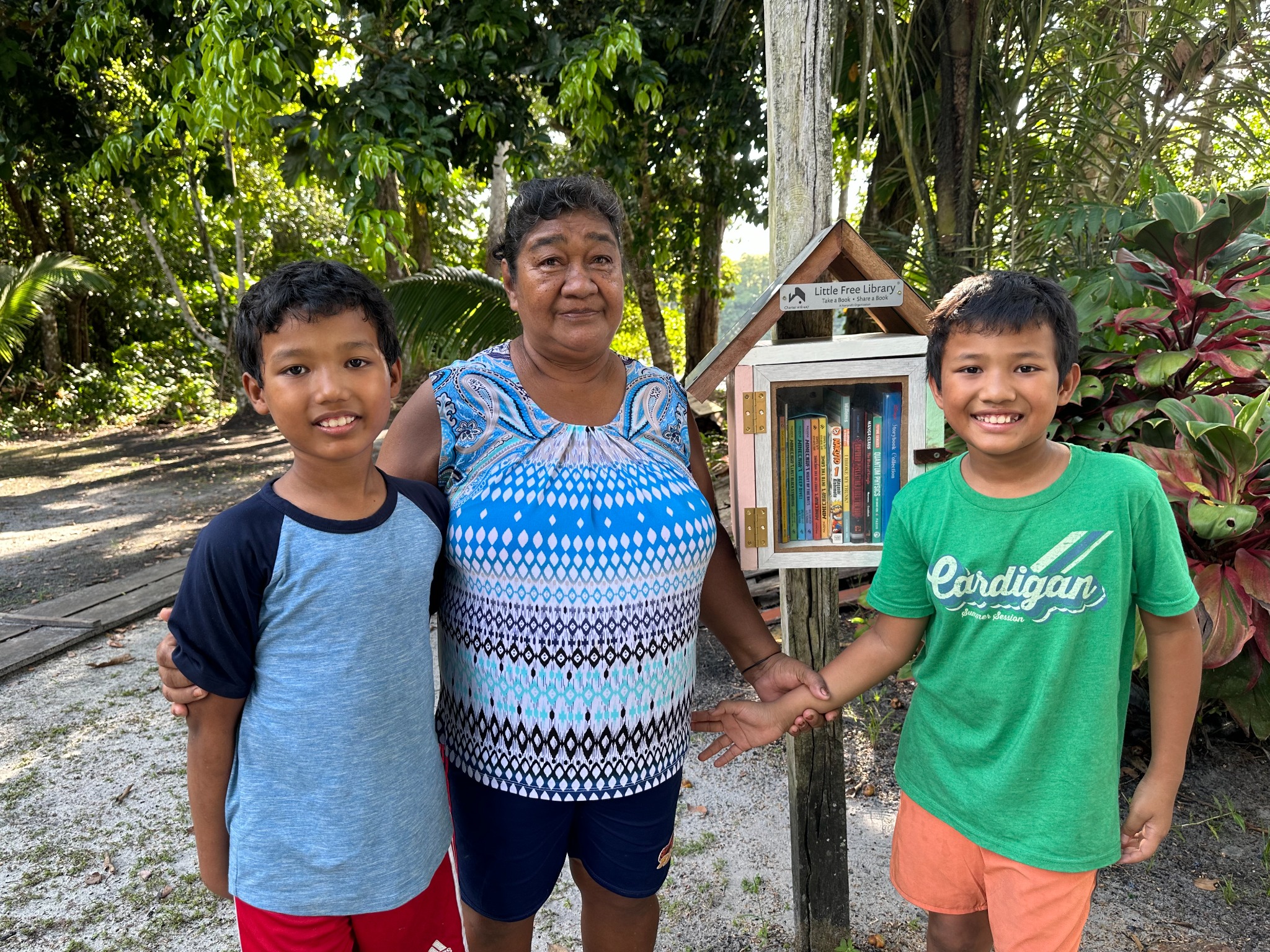 The two young builders with a community member beside the library